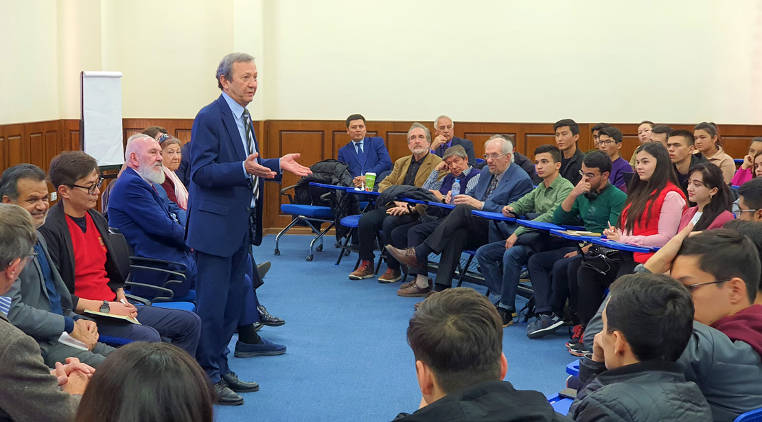 Speaker stands and gives talk in large classroom group of seated attendees.