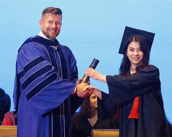 Ryan Guffey hands diploma to graduating Tashkent student.
