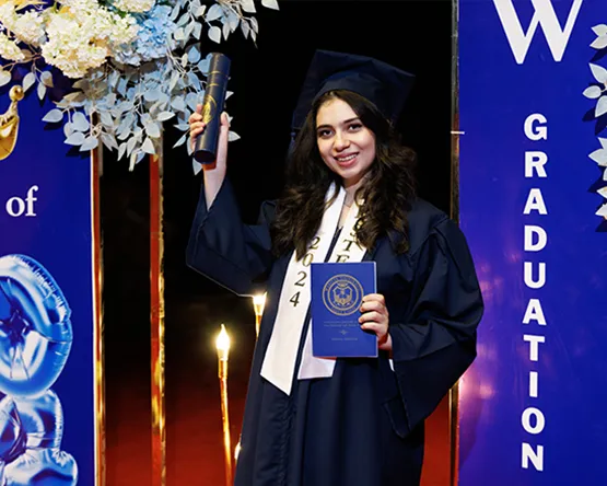 Graduating student in cap and gown holding commencement program and diploma.