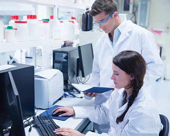 Students wearing white lab coats work on computer