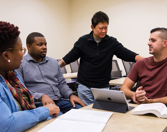 Students talking in a group, one standing, three sitting.