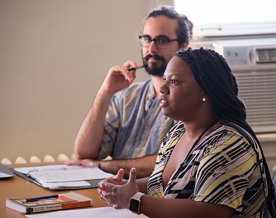 Two students sitting in a classroom; one is speaking, the other is listening closely